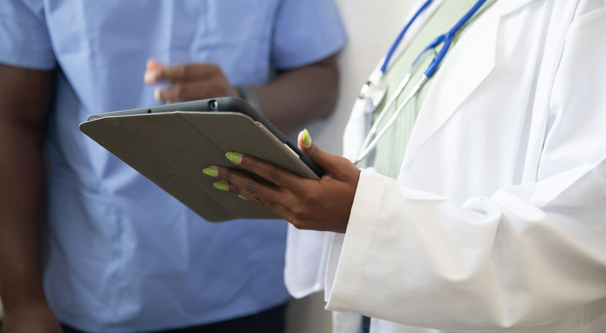 A doctor in a white coat holding a tablet, a colleague in scrubs alongside
